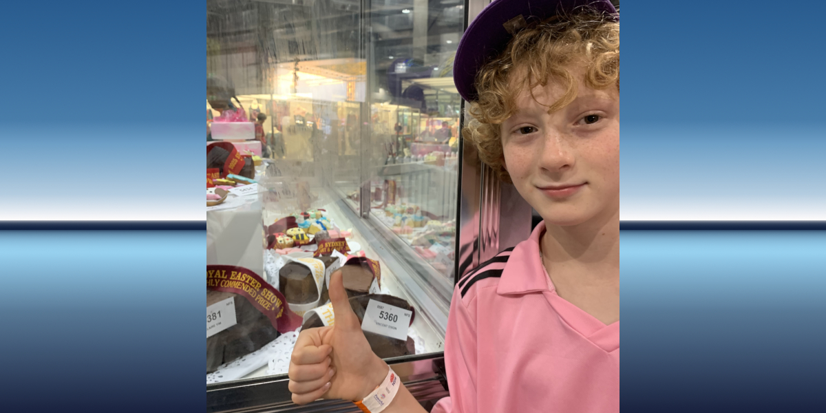 Royal Easter Show Cake Competition winner standing in from of glass cabinet containing cakes
