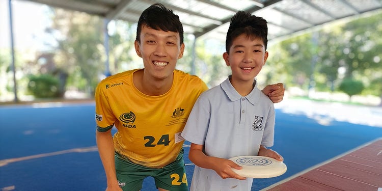 student posing for photo with frisbee team member on oval